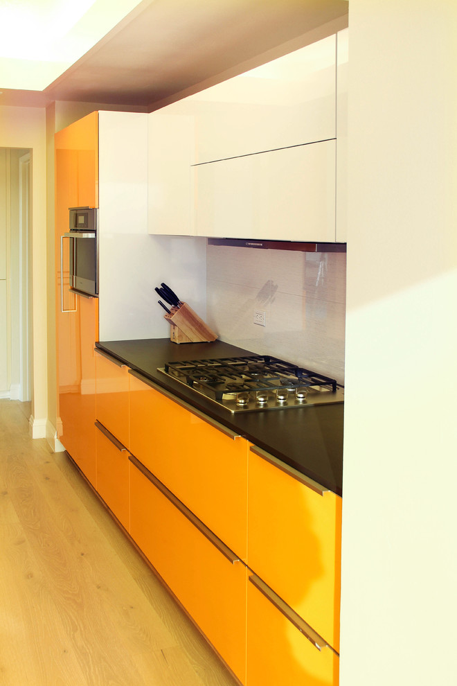 Small modern single-wall eat-in kitchen in Los Angeles with a drop-in sink, flat-panel cabinets, orange cabinets, quartz benchtops, black splashback, porcelain splashback, stainless steel appliances, light hardwood floors and no island.