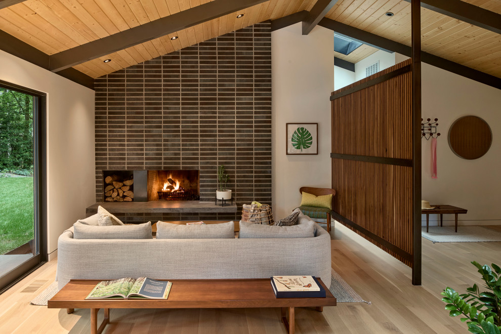 Photo of a midcentury open concept living room in Portland with light hardwood floors, a standard fireplace, a tile fireplace surround, exposed beam, white walls, no tv and brown floor.