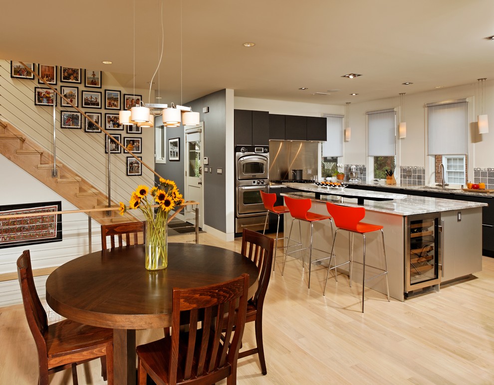Mid-sized transitional l-shaped eat-in kitchen in DC Metro with a single-bowl sink, flat-panel cabinets, black cabinets, granite benchtops, metallic splashback, metal splashback, stainless steel appliances, light hardwood floors, with island and beige floor.