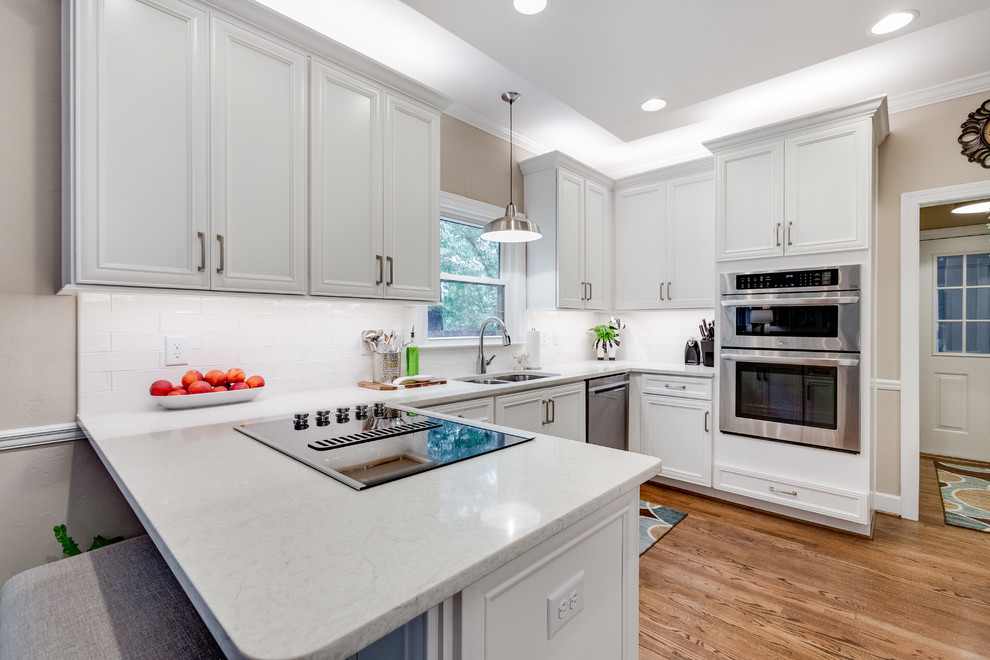Inspiration for a mid-sized transitional u-shaped medium tone wood floor and brown floor eat-in kitchen remodel in Birmingham with a double-bowl sink, recessed-panel cabinets, white cabinets, quartz countertops, white backsplash, subway tile backsplash, stainless steel appliances, a peninsula and white countertops