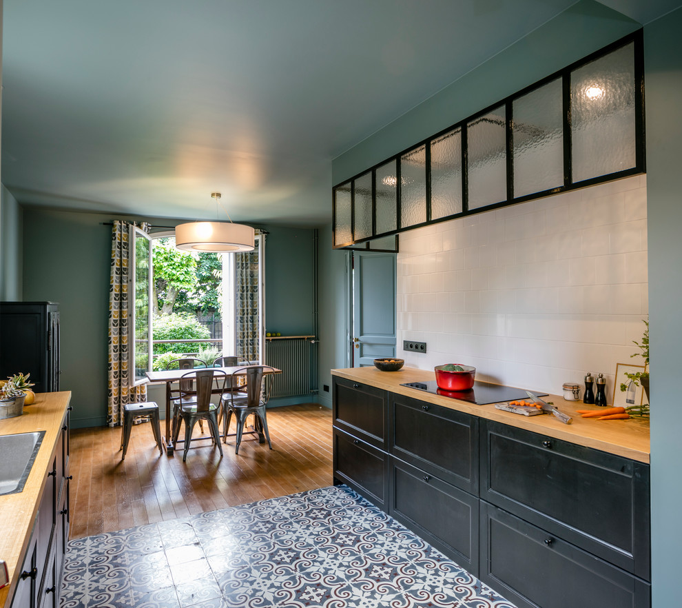Photo of a mid-sized contemporary galley kitchen in Paris with black cabinets, wood benchtops, white splashback, matchstick tile splashback, ceramic floors and beige benchtop.
