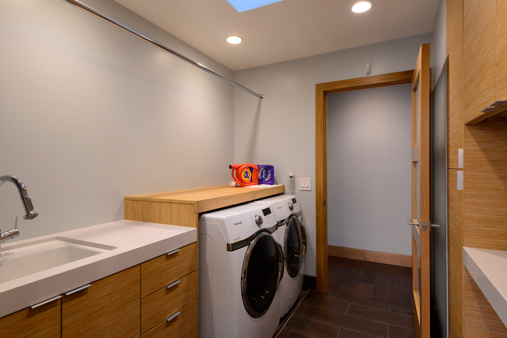Design ideas for a mid-sized contemporary galley dedicated laundry room in Orange County with an undermount sink, flat-panel cabinets, solid surface benchtops, white walls, dark hardwood floors, a side-by-side washer and dryer and medium wood cabinets.