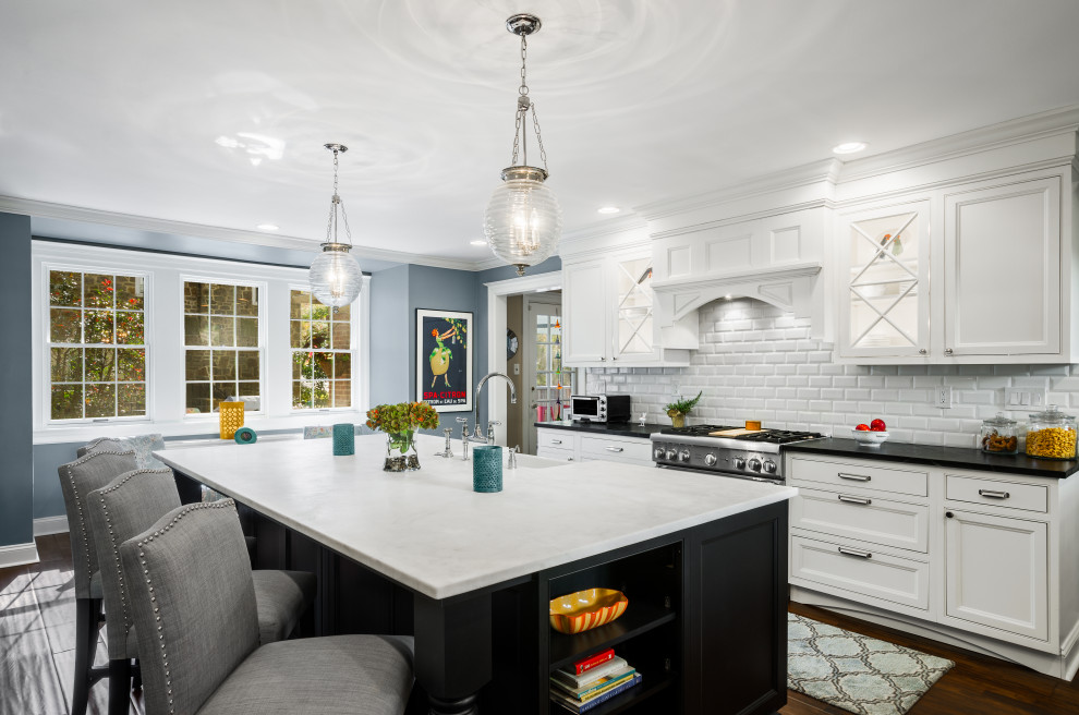 Photo of a large traditional l-shaped eat-in kitchen in Philadelphia with a farmhouse sink, beaded inset cabinets, black cabinets, quartz benchtops, white splashback, subway tile splashback, stainless steel appliances, dark hardwood floors, with island, brown floor and white benchtop.