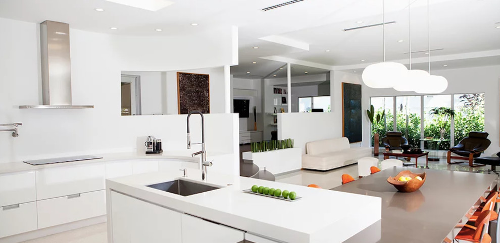 Large modern u-shaped open plan kitchen with an undermount sink, flat-panel cabinets, white cabinets, solid surface benchtops, stainless steel appliances, porcelain floors, with island, beige floor and white benchtop.