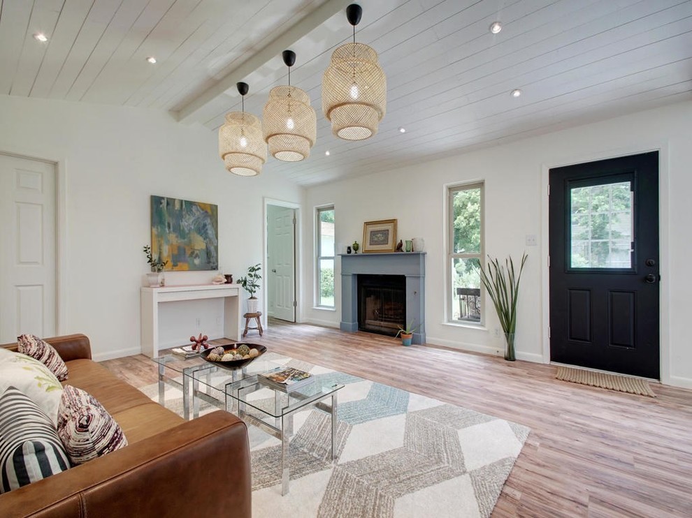 This is an example of a mid-sized country open concept living room in Austin with white walls, laminate floors, a wood stove, a wood fireplace surround and brown floor.