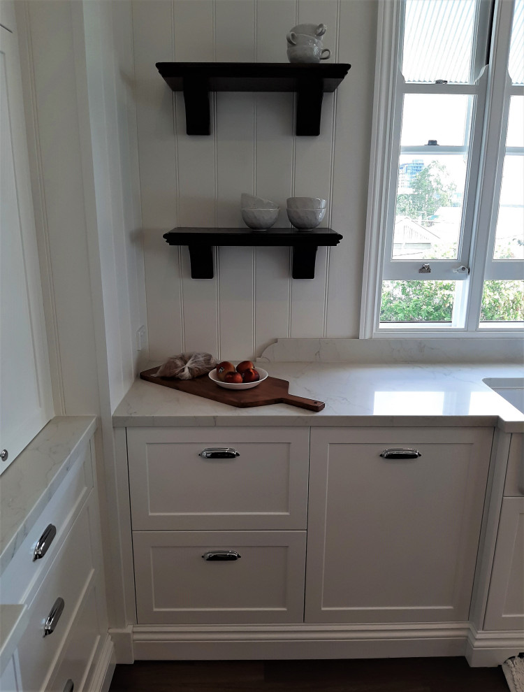 This is an example of a large transitional u-shaped kitchen pantry in Brisbane with a farmhouse sink, shaker cabinets, white cabinets, quartz benchtops, white splashback, subway tile splashback, medium hardwood floors, with island and white benchtop.