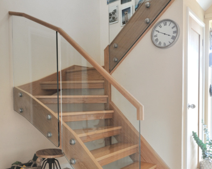 Mid-sized contemporary wood u-shaped staircase in Cardiff with glass risers and wood railing.