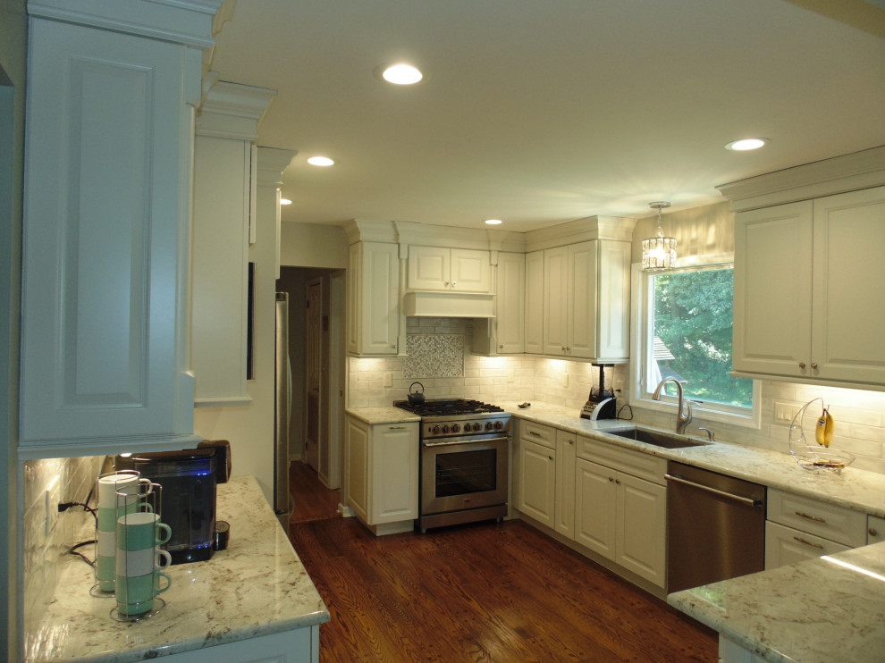 Mid-sized transitional u-shaped medium tone wood floor and brown floor eat-in kitchen photo with an undermount sink, raised-panel cabinets, white cabinets, granite countertops, white backsplash, subway tile backsplash, stainless steel appliances, no island and gray countertops