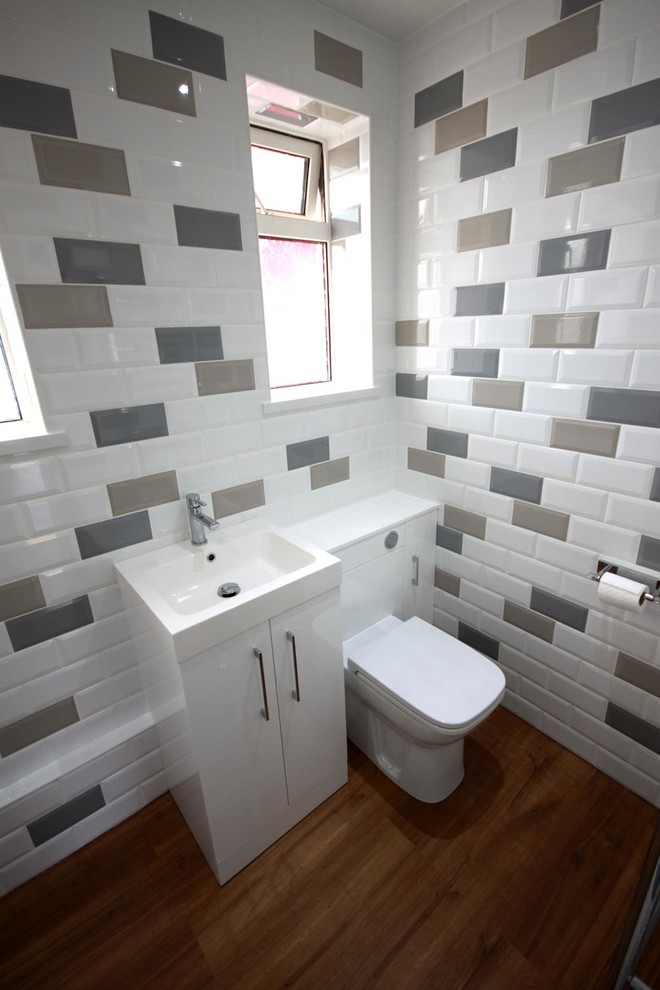 Inspiration for a mid-sized contemporary kids bathroom in Other with furniture-like cabinets, white cabinets, a corner tub, a shower/bathtub combo, a one-piece toilet, multi-coloured tile, ceramic tile, white walls, laminate floors, an integrated sink and brown floor.