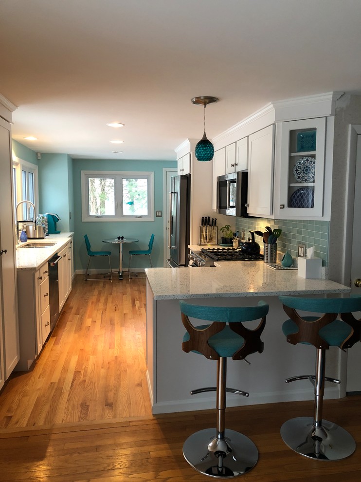 Design ideas for a mid-sized transitional galley eat-in kitchen in Providence with a double-bowl sink, glass tile splashback, stainless steel appliances, a peninsula, shaker cabinets, white cabinets, tile benchtops, blue splashback, medium hardwood floors, brown floor and white benchtop.