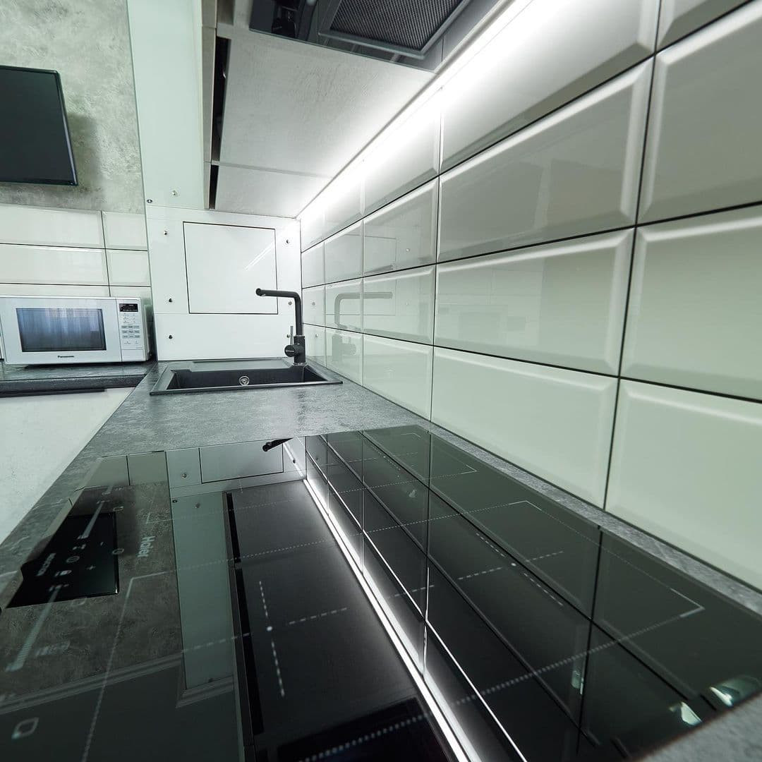 Белая угловая кухня с высокими шкафами и черной столешницей