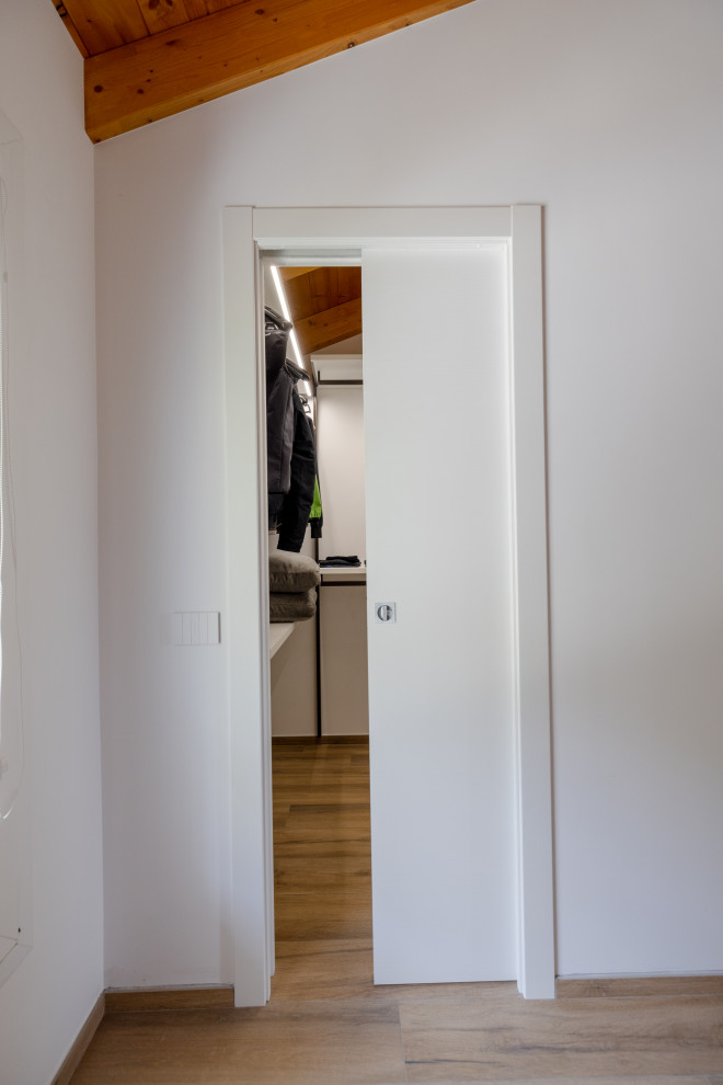 Immagine di una piccola cabina armadio unisex contemporanea con nessun'anta, ante bianche, pavimento in legno verniciato, pavimento marrone e travi a vista