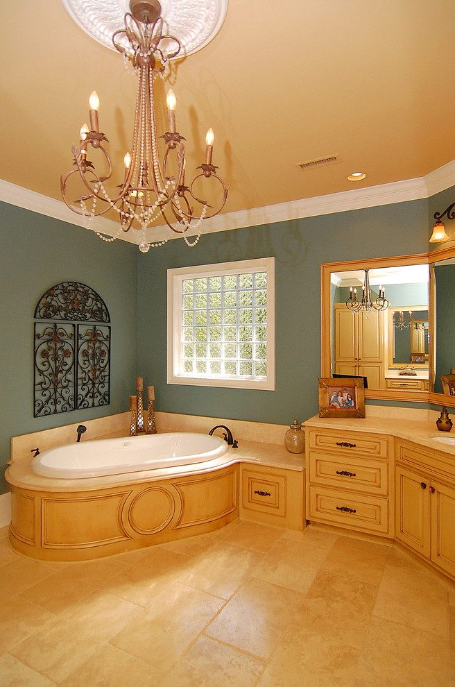This is an example of a large traditional master bathroom in Charleston with raised-panel cabinets, yellow cabinets, a drop-in tub, a corner shower, beige tile, blue walls, ceramic floors, an undermount sink, granite benchtops, beige floor and a hinged shower door.