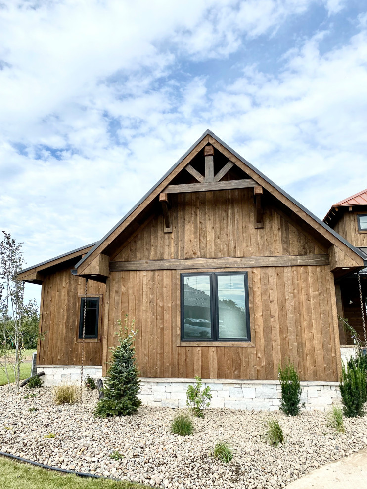 This is an example of a large country one-storey brown house exterior in Kansas City with wood siding, a gable roof, a metal roof and a black roof.