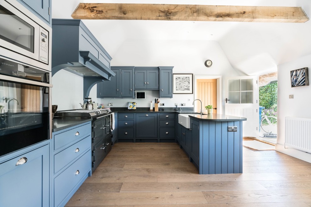 Design ideas for a large country u-shaped eat-in kitchen in Cambridgeshire with a farmhouse sink, blue cabinets, quartzite benchtops, medium hardwood floors, a peninsula, grey benchtop, recessed-panel cabinets, white splashback and brown floor.
