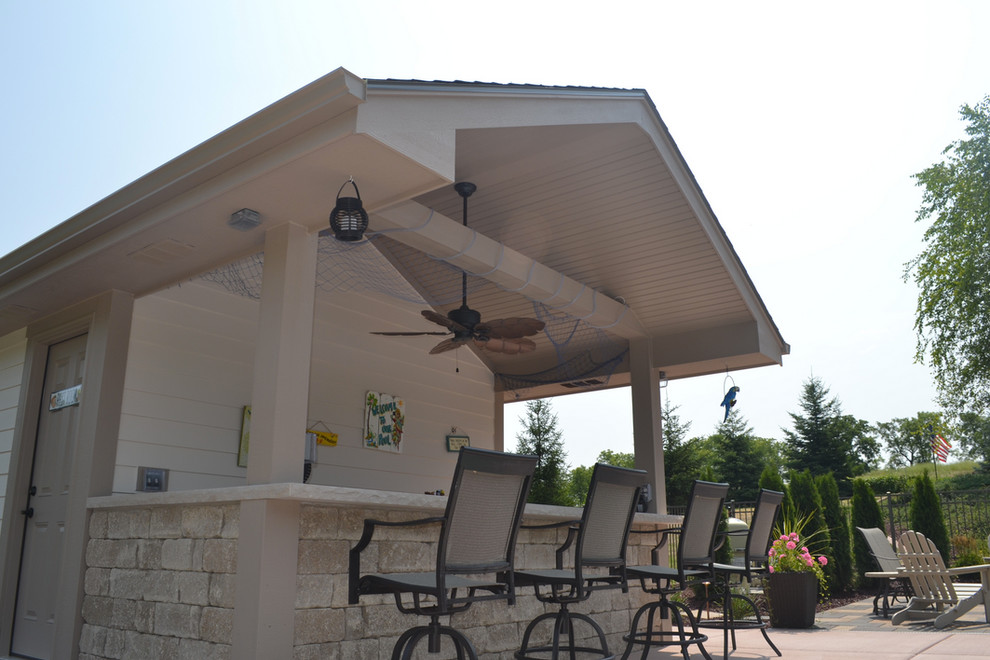 This is an example of a large traditional backyard patio in Milwaukee with an outdoor kitchen, concrete slab and a roof extension.