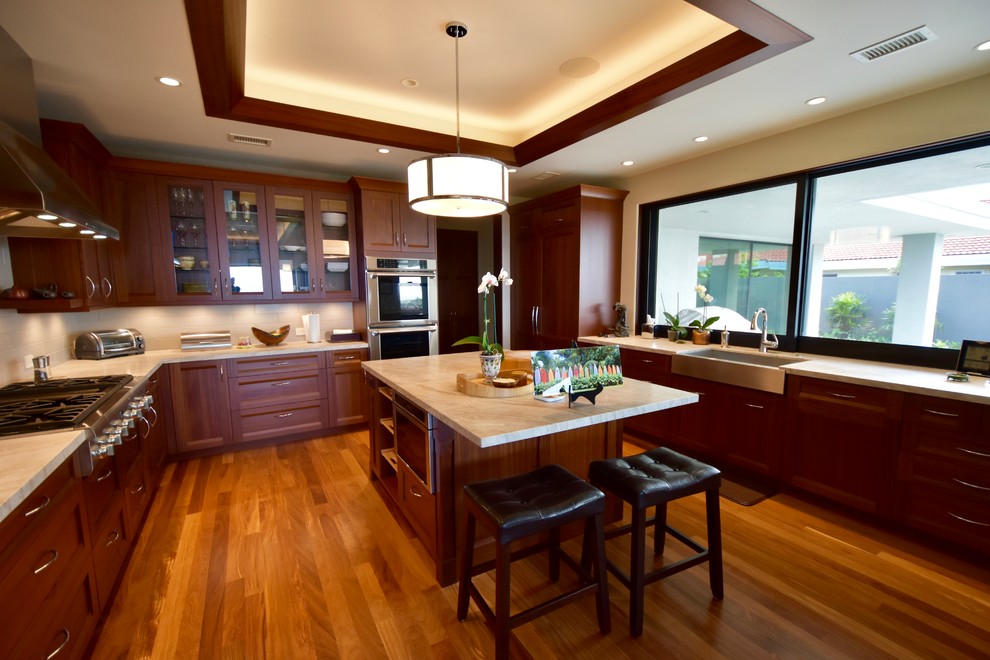 Design ideas for a large tropical u-shaped open plan kitchen in Hawaii with a single-bowl sink, recessed-panel cabinets, dark wood cabinets, marble benchtops, beige splashback, ceramic splashback, stainless steel appliances, medium hardwood floors and with island.