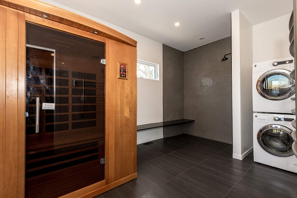 This is an example of a large contemporary single-wall dedicated laundry room in Ottawa with white walls, porcelain floors, a stacked washer and dryer and grey floor.