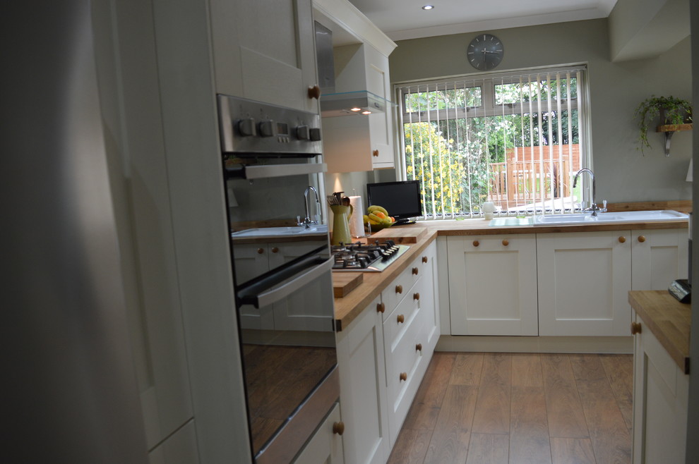 Mid-sized eat-in kitchen in Other with shaker cabinets, white cabinets, wood benchtops, metallic splashback, metal splashback, stainless steel appliances, laminate floors and no island.
