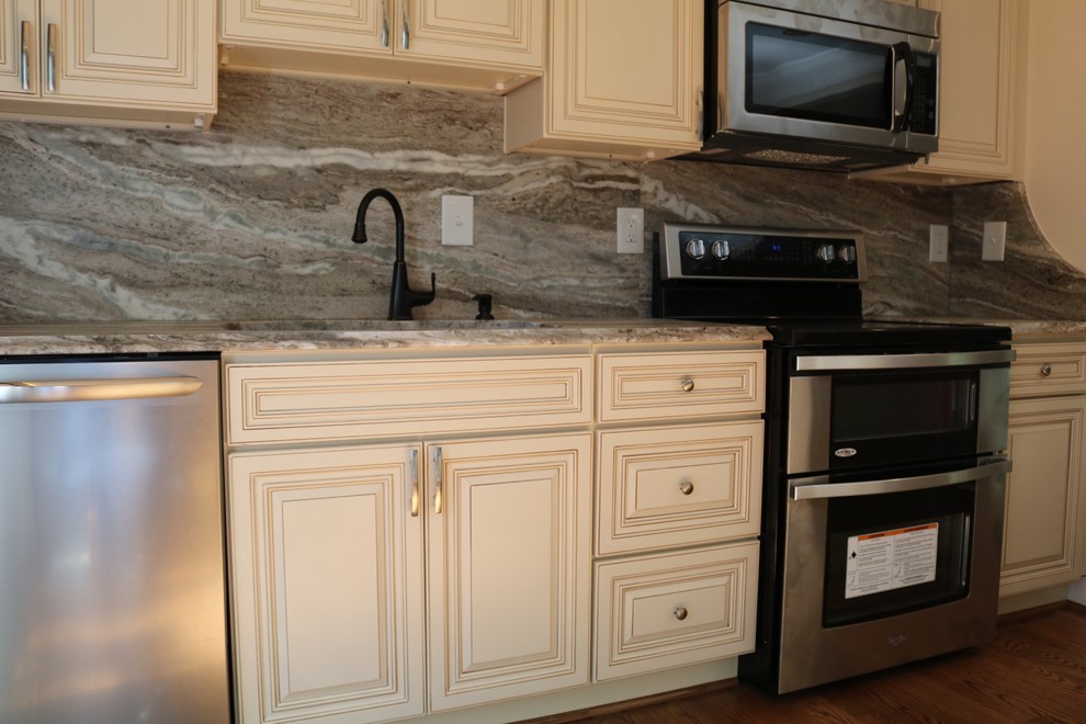 Example of a mid-sized transitional l-shaped kitchen design in DC Metro with an undermount sink, raised-panel cabinets, white cabinets, granite countertops, gray backsplash, stainless steel appliances and an island