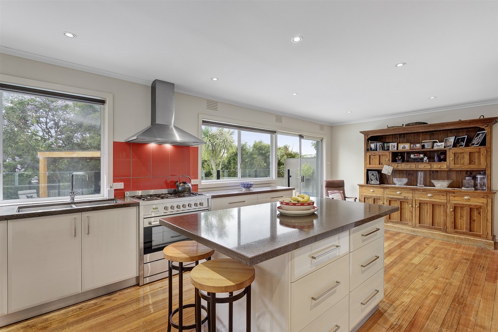 Contemporary kitchen in Melbourne with a double-bowl sink, flat-panel cabinets, white cabinets, red splashback, stainless steel appliances, light hardwood floors and with island.