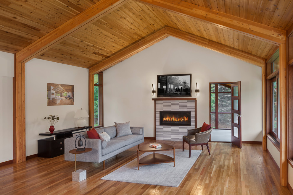 Mid-sized midcentury open concept living room in Boston with white walls, medium hardwood floors, a ribbon fireplace, a tile fireplace surround, a wall-mounted tv and brown floor.