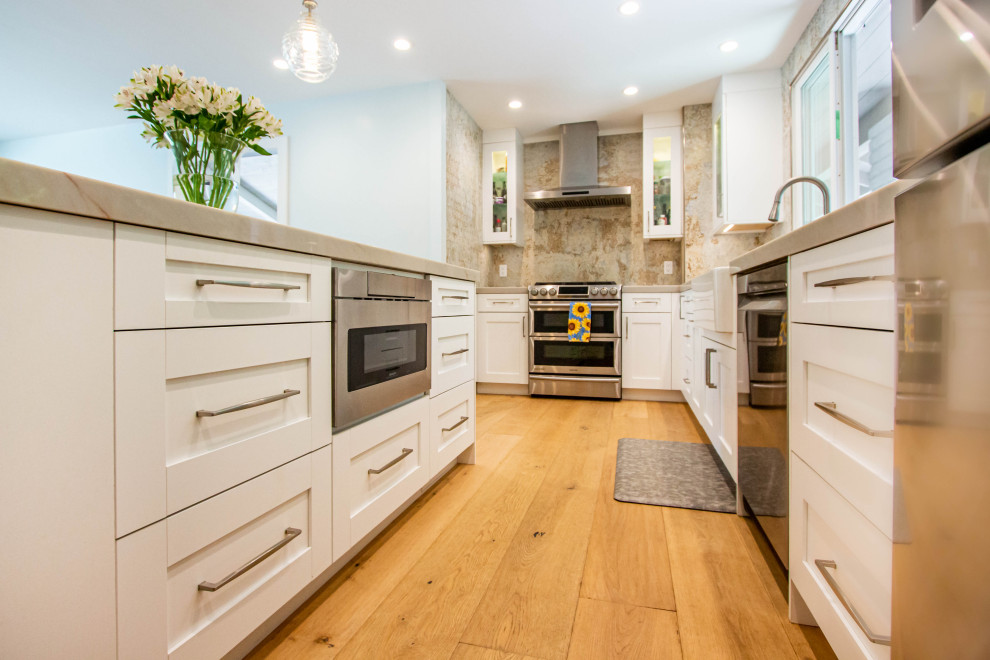 Inspiration for a transitional l-shaped light wood floor and brown floor eat-in kitchen remodel with a farmhouse sink, shaker cabinets, white cabinets, quartz countertops, porcelain backsplash, stainless steel appliances and an island