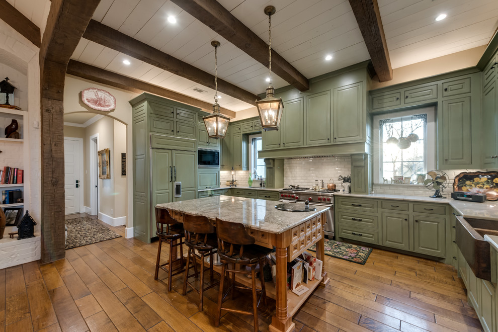 Design ideas for a large traditional l-shaped eat-in kitchen in Dallas with a drop-in sink, shaker cabinets, green cabinets, quartzite benchtops, white splashback, subway tile splashback, stainless steel appliances, medium hardwood floors, with island and brown floor.