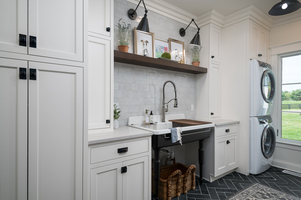 Inspiration for a large transitional galley dedicated laundry room in Other with a single-bowl sink, flat-panel cabinets, white cabinets, quartz benchtops, white splashback, porcelain splashback, white walls, slate floors, a stacked washer and dryer, black floor and white benchtop.