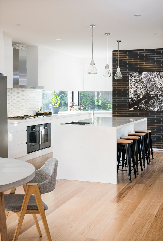 Large contemporary l-shaped kitchen pantry in Melbourne with a drop-in sink, flat-panel cabinets, white cabinets, quartz benchtops, white splashback, cement tile splashback, black appliances, medium hardwood floors and with island.