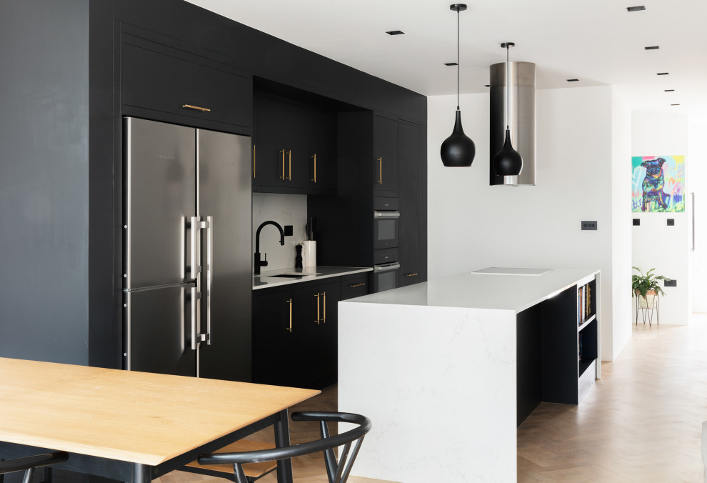 Contemporary single-wall open plan kitchen in London with flat-panel cabinets, black cabinets, white splashback, medium hardwood flooring and an island.