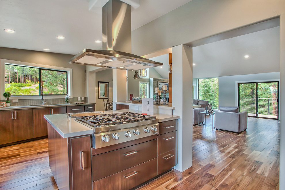 Example of a trendy u-shaped medium tone wood floor open concept kitchen design with an undermount sink, flat-panel cabinets, medium tone wood cabinets, limestone countertops, gray backsplash, glass tile backsplash, paneled appliances and an island