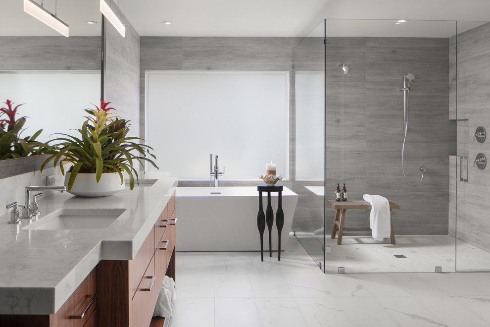 Design ideas for a contemporary bathroom in Orlando with flat-panel cabinets, medium wood cabinets, a freestanding tub, a curbless shower, gray tile, grey walls, an undermount sink, white floor, a hinged shower door and white benchtops.