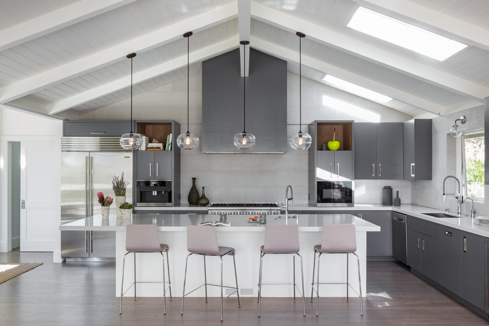 This is an example of a large beach style l-shaped open plan kitchen in San Francisco with a single-bowl sink, flat-panel cabinets, grey cabinets, grey splashback, stainless steel appliances, dark hardwood floors, with island, brown floor, quartz benchtops and ceramic splashback.