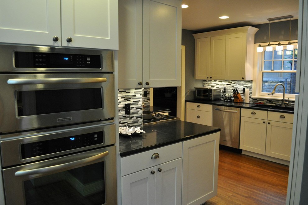 Example of a transitional dark wood floor eat-in kitchen design with shaker cabinets, white cabinets, granite countertops, multicolored backsplash, glass tile backsplash and stainless steel appliances