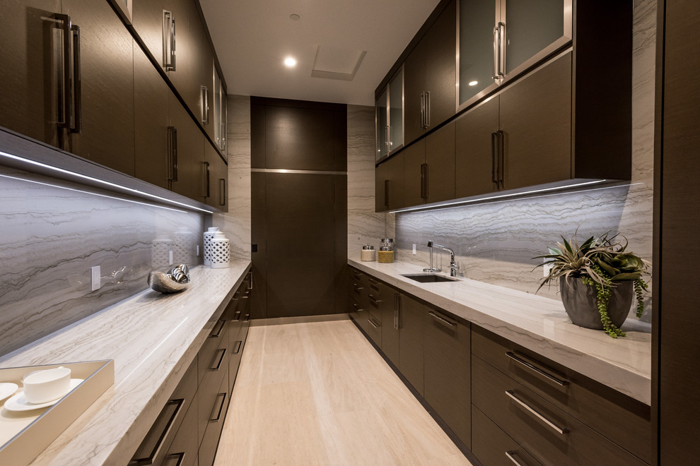 Inspiration for a large contemporary galley kitchen pantry in Las Vegas with an undermount sink, flat-panel cabinets, dark wood cabinets, granite benchtops, grey splashback, stone slab splashback, stainless steel appliances, limestone floors, with island, beige floor and beige benchtop.