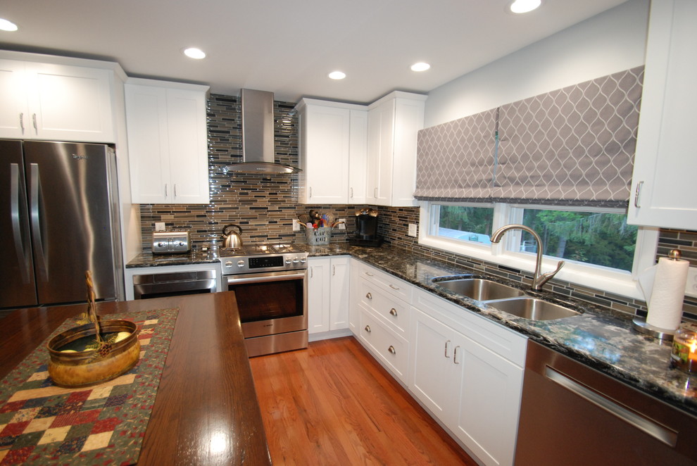 Mid-sized transitional l-shaped kitchen in New York with a double-bowl sink, shaker cabinets, white cabinets, quartz benchtops, beige splashback, glass sheet splashback, stainless steel appliances, medium hardwood floors, with island and brown floor.