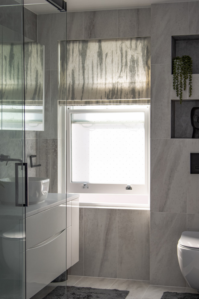 Bild på ett mellanstort funkis vit vitt en-suite badrum, med släta luckor, vita skåp, en kantlös dusch, en vägghängd toalettstol, grå kakel, porslinskakel, grå väggar, klinkergolv i porslin, ett konsol handfat, marmorbänkskiva, vitt golv och dusch med skjutdörr