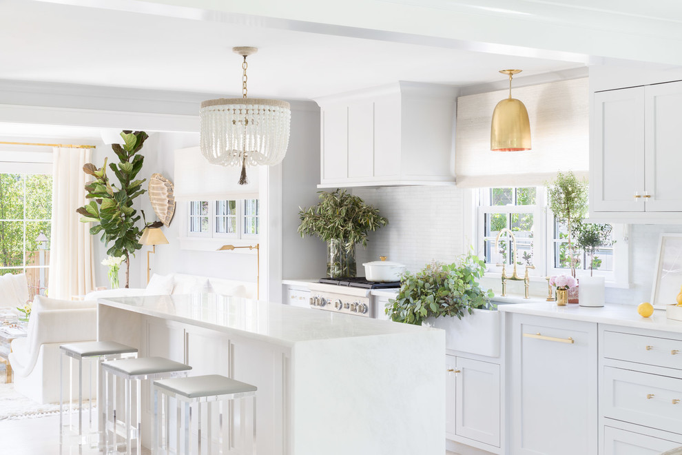 Photo of a beach style open plan kitchen in New York with a farmhouse sink, shaker cabinets, white cabinets, white splashback, stainless steel appliances and with island.