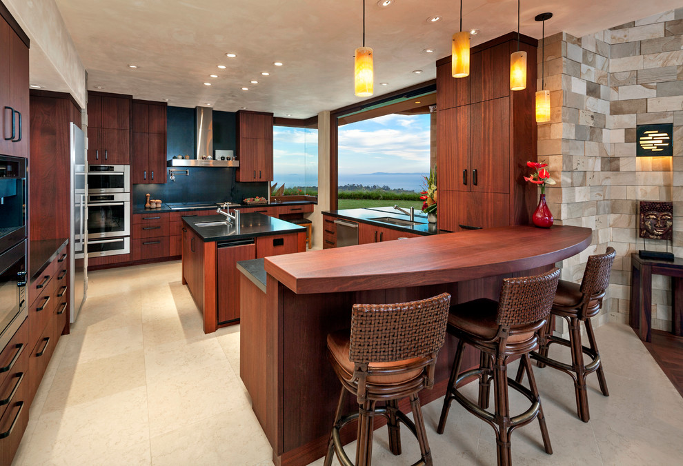 Design ideas for a large tropical u-shaped open plan kitchen in Santa Barbara with an undermount sink, flat-panel cabinets, dark wood cabinets, granite benchtops, black splashback, stone slab splashback, stainless steel appliances, limestone floors and with island.