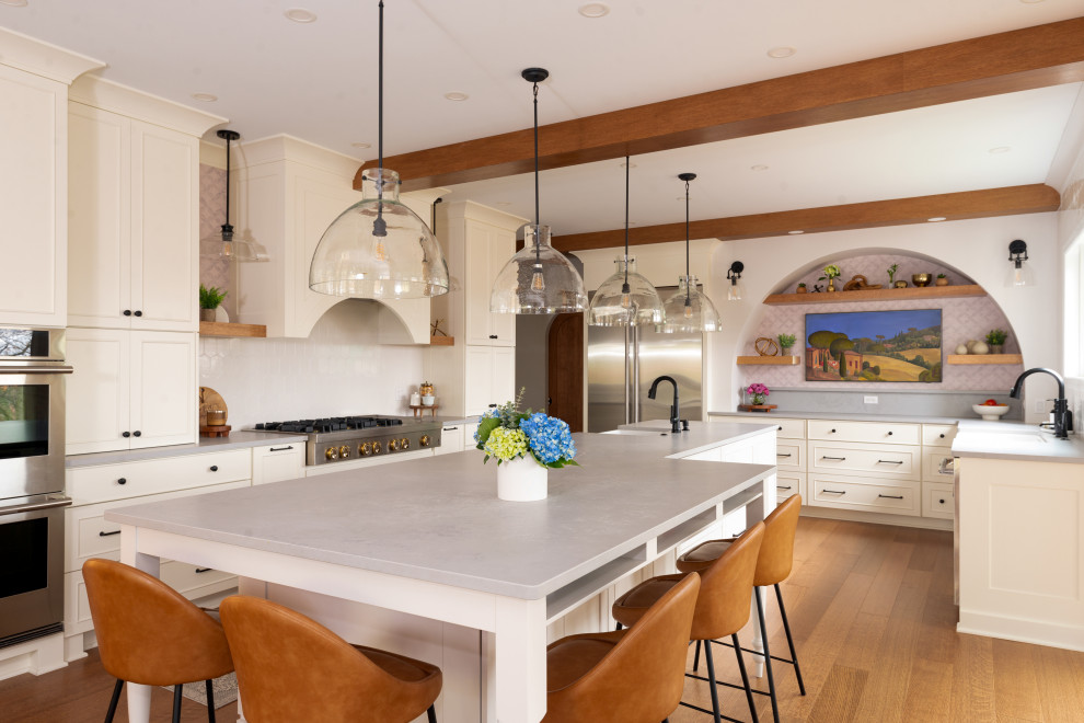 Example of a large transitional medium tone wood floor and exposed beam eat-in kitchen design with white backsplash, stainless steel appliances and an island