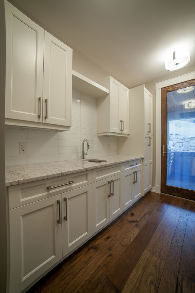 Photo of a mid-sized contemporary single-wall kitchen pantry in Vancouver with an undermount sink, shaker cabinets, white cabinets, granite benchtops, white splashback, ceramic splashback, medium hardwood floors and no island.