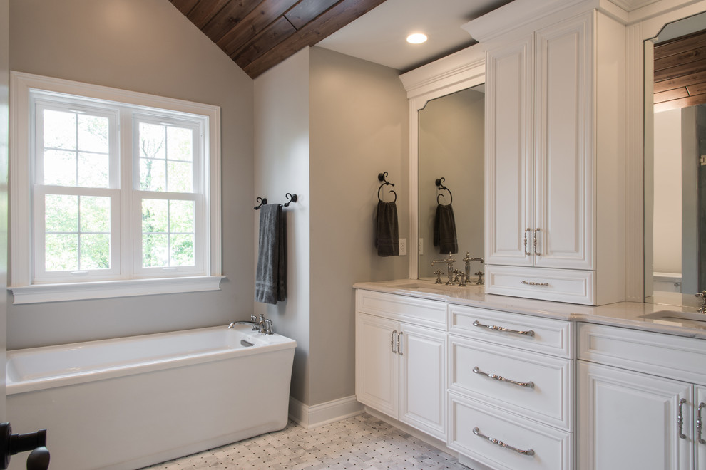 Mid-sized transitional master bathroom in St Louis with raised-panel cabinets, white cabinets, a freestanding tub, an alcove shower, a one-piece toilet, white tile, marble, beige walls, marble floors, an undermount sink, engineered quartz benchtops, white floor and a hinged shower door.