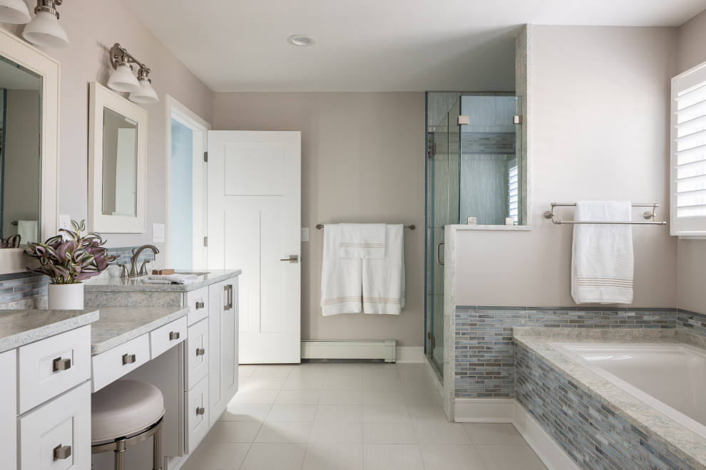 Photo of a large beach style master bathroom in New York with recessed-panel cabinets, white cabinets, a drop-in tub, a corner shower, blue tile, glass sheet wall, beige walls, porcelain floors, an undermount sink, engineered quartz benchtops, beige floor, a hinged shower door, multi-coloured benchtops, a double vanity and a built-in vanity.