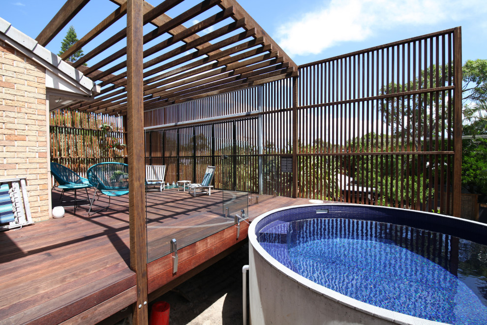 Mid-sized urban ground level privacy and wood railing deck photo in Sunshine Coast with a pergola