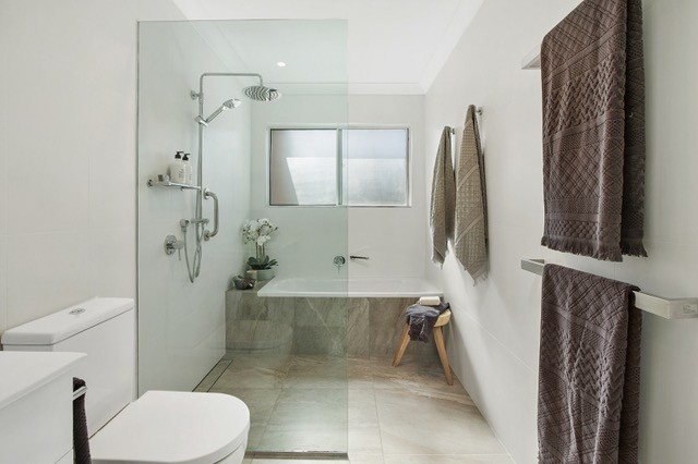 Inspiration for a mid-sized contemporary bathroom in Sydney with flat-panel cabinets, white cabinets, an alcove tub, an open shower, a two-piece toilet, beige tile, ceramic tile, white walls, ceramic floors, a trough sink and solid surface benchtops.