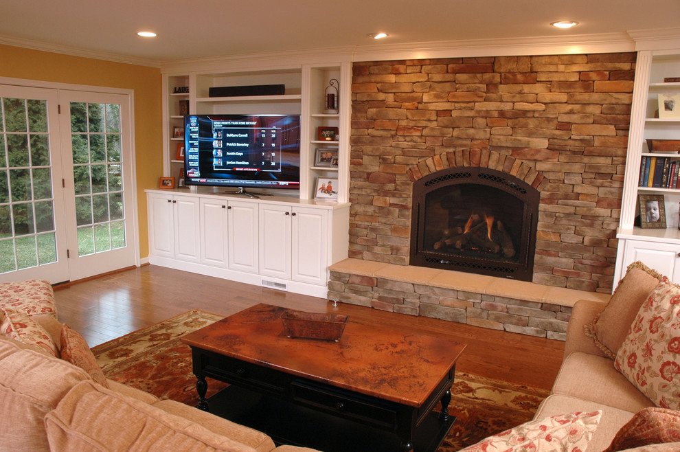 Photo of a mid-sized traditional open concept family room in Cincinnati with yellow walls, medium hardwood floors, a standard fireplace, a stone fireplace surround and a freestanding tv.