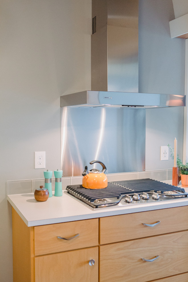 Small midcentury galley separate kitchen in Grand Rapids with a drop-in sink, flat-panel cabinets, light wood cabinets, laminate benchtops, grey splashback, glass tile splashback, stainless steel appliances, medium hardwood floors, no island, grey floor and beige benchtop.
