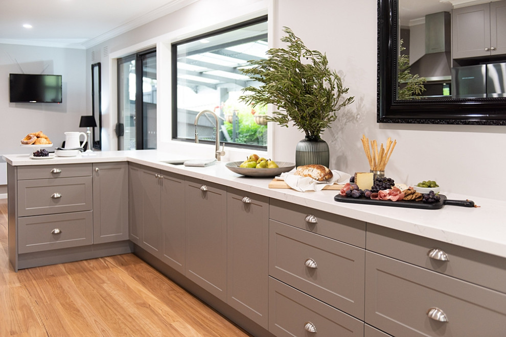 Photo of a large traditional galley kitchen pantry in Melbourne with a submerged sink, shaker cabinets, grey cabinets, composite countertops, white splashback, stainless steel appliances, medium hardwood flooring, an island, beige floors and white worktops.