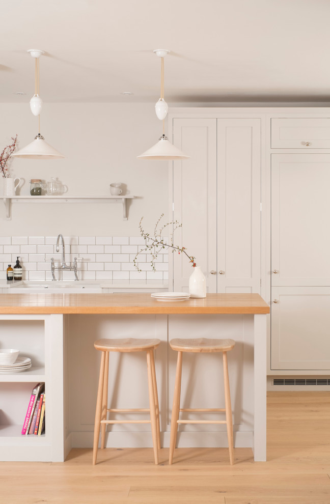 Mid-sized traditional l-shaped open plan kitchen in Cardiff with a farmhouse sink, shaker cabinets, white cabinets, quartzite benchtops, white splashback, subway tile splashback, stainless steel appliances, medium hardwood floors and with island.